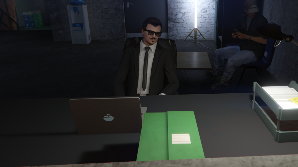 A man in a suit working on a laptop at a desk in a dark bunker.