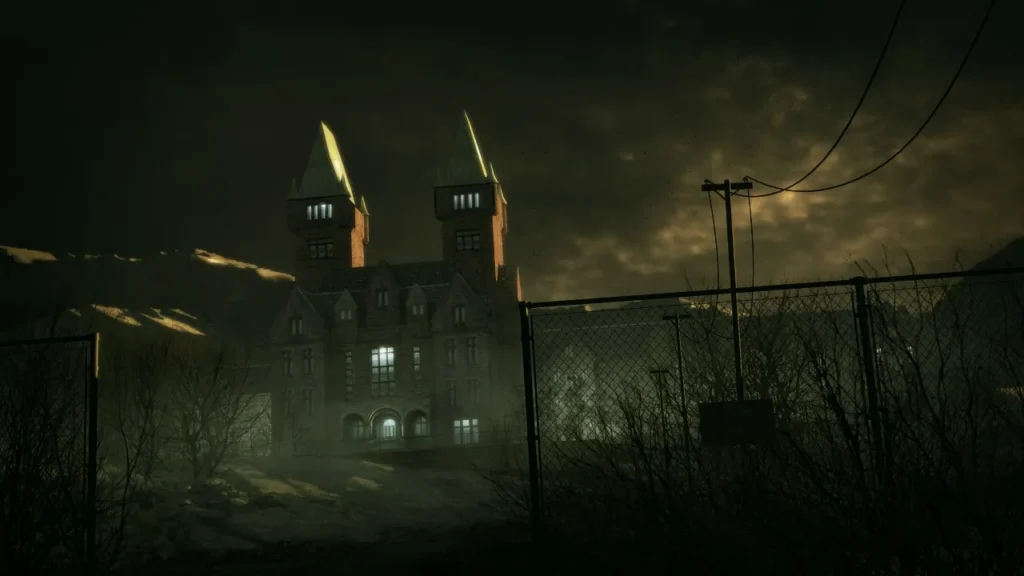 A dark, moody shot of the Mount Massive Asylum building at night, surrounded by a chain-link fence under a cloudy sky.